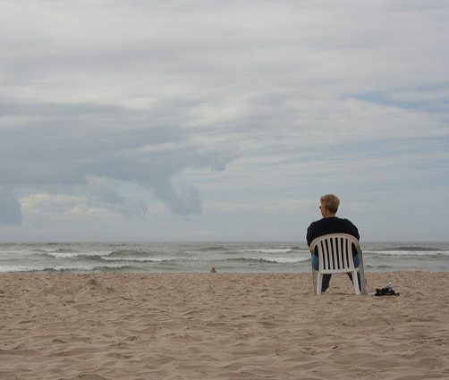 man sitting alone in chair on beach
